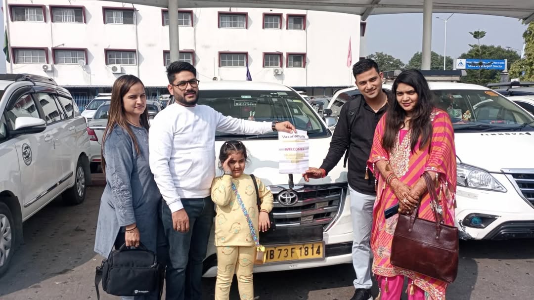 A group of travelers posing with a white Toyota Innova taxi for a tour service in West Bengal, India.