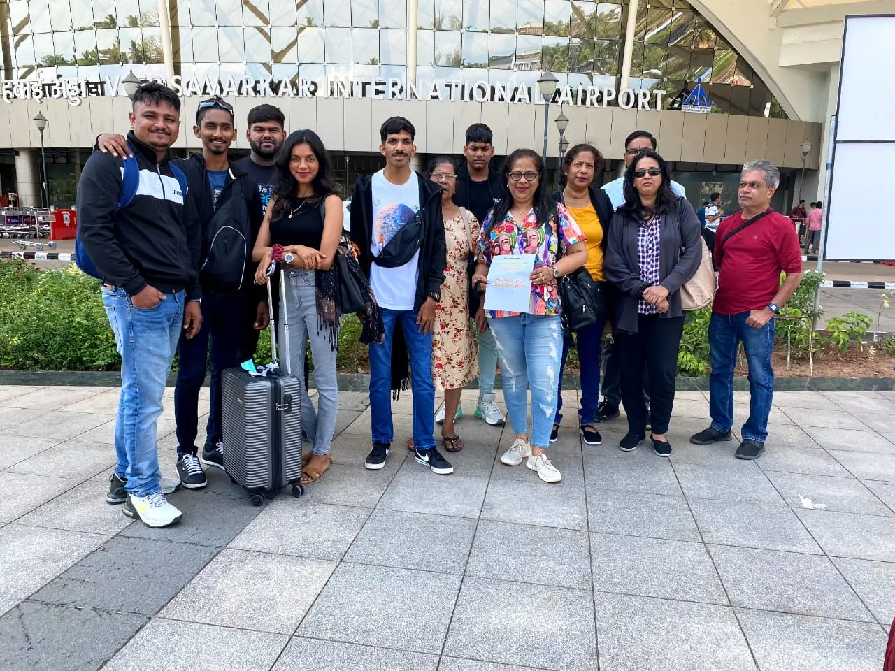 A group of eleven people pose for a photo outside the terminal building of the Veer Savarkar International Airport