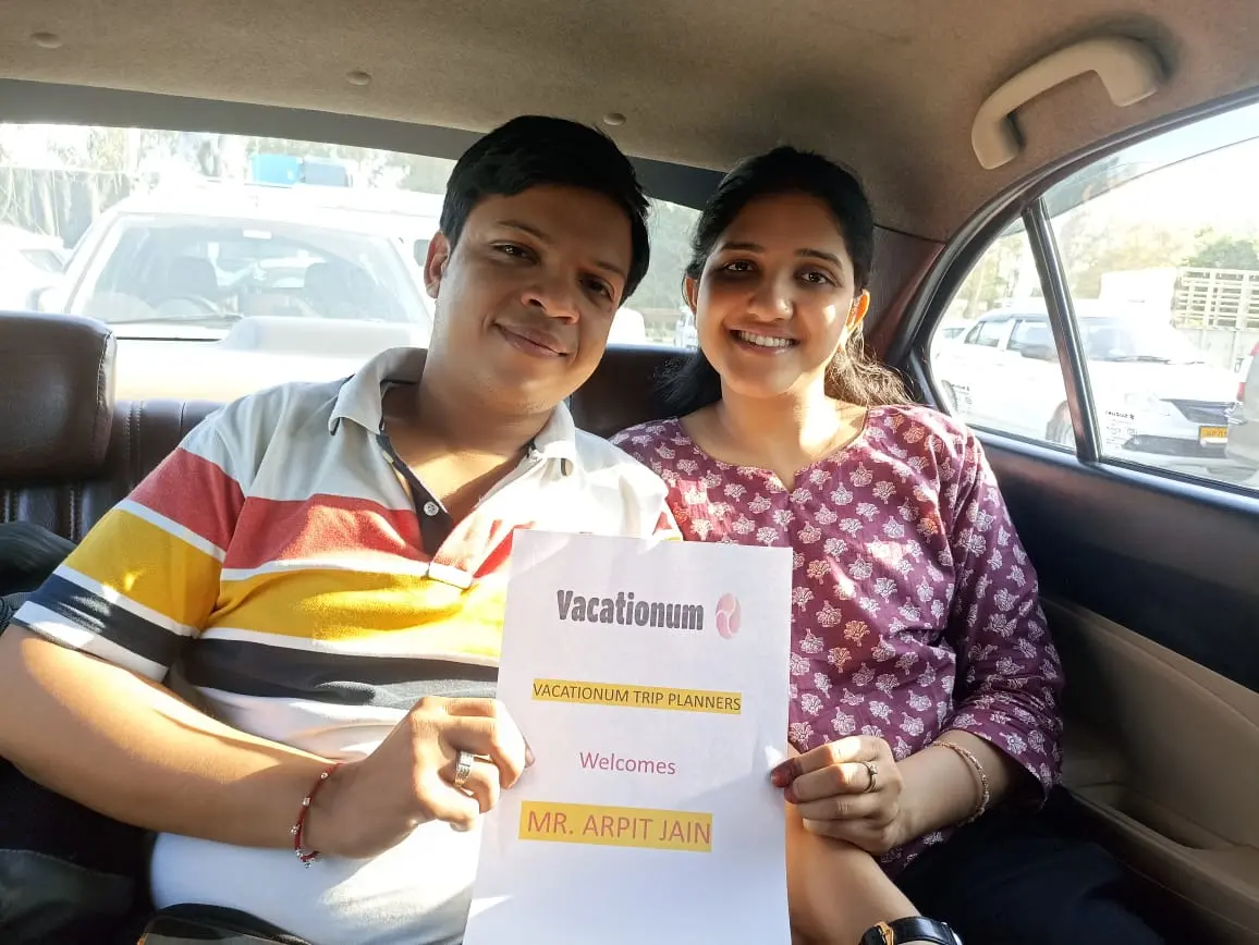A couple holding a welcome sign from Vacationum while sitting in the back of a car.