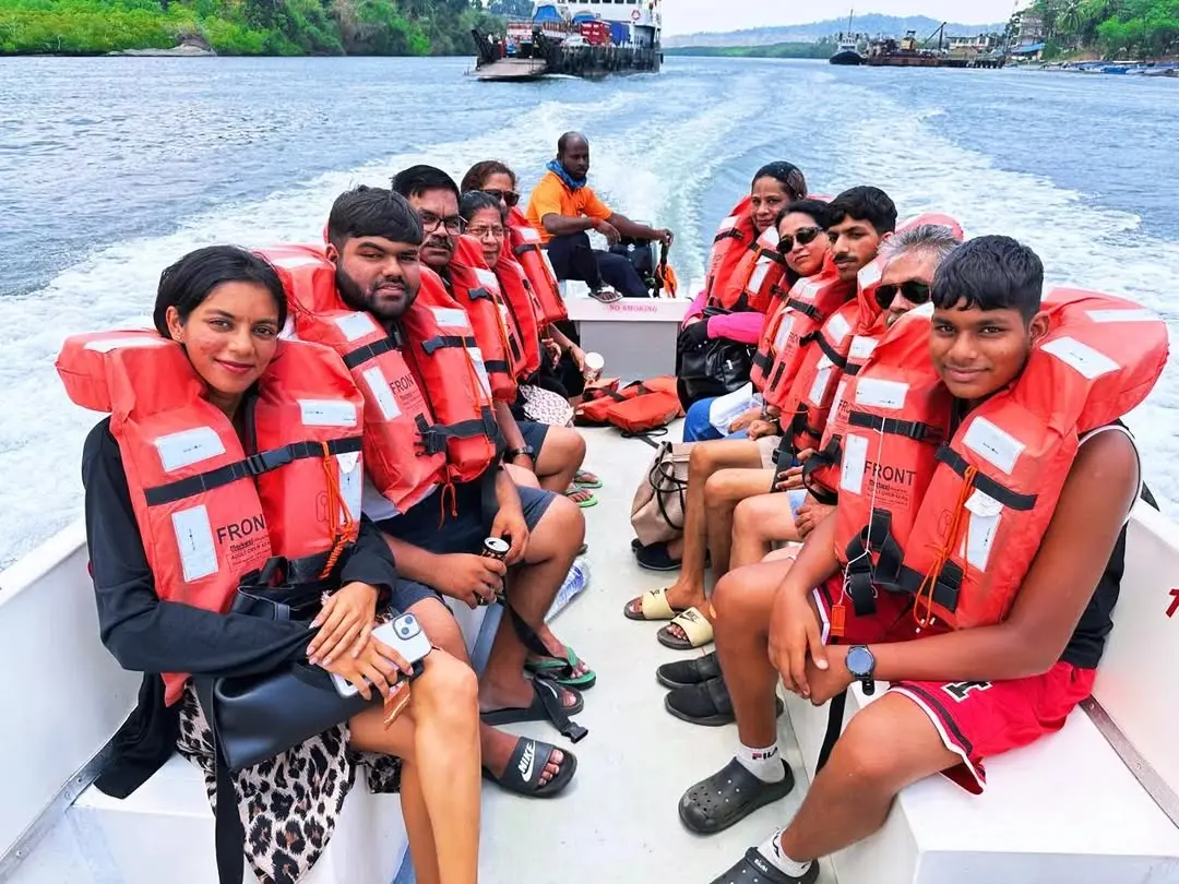 A group of diverse travelers wearing bright orange life jackets sit on a white boat during a scenic water excursion.
