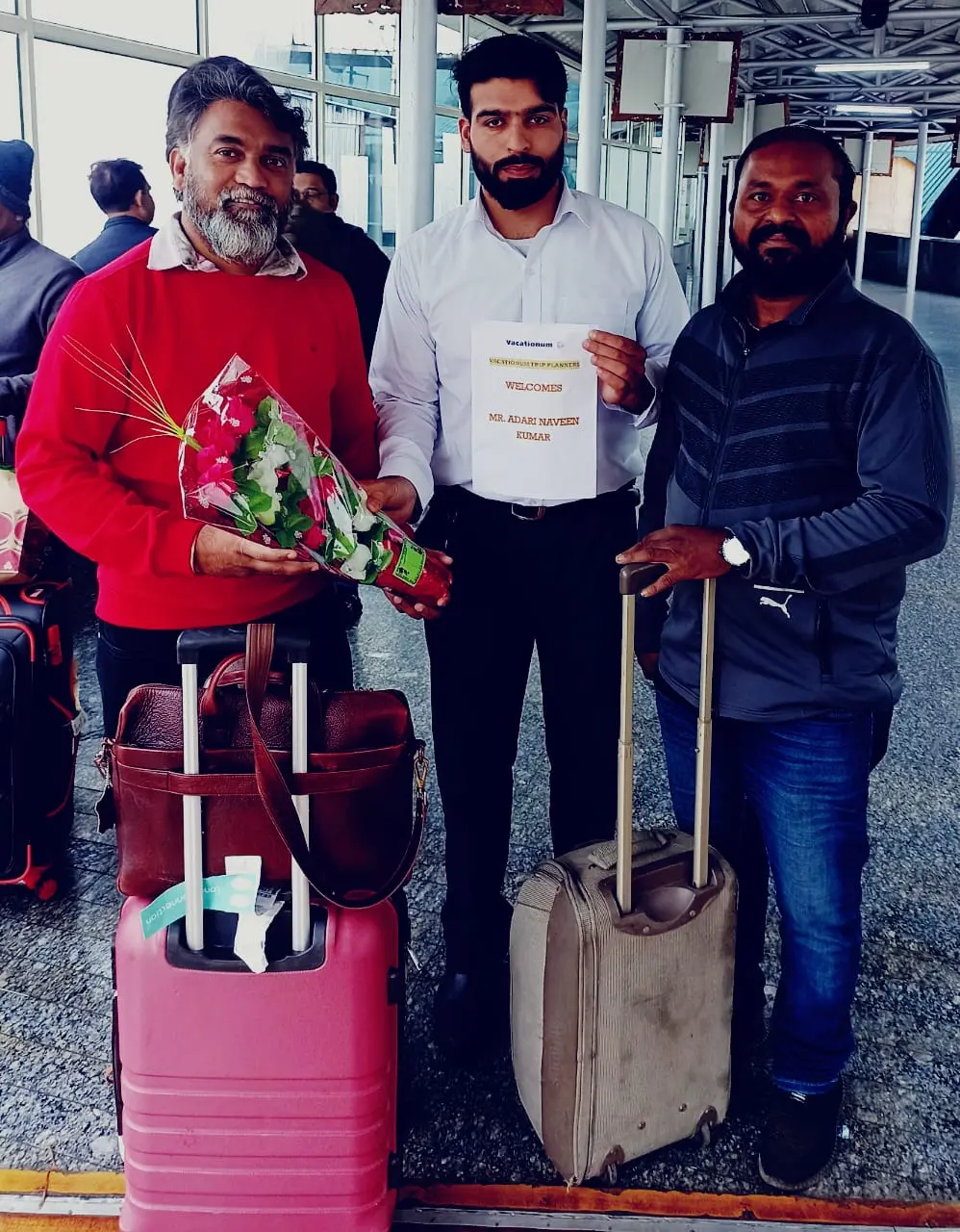 Two men holding Vacationum Trip Planners welcome placard at Srinagar airport.