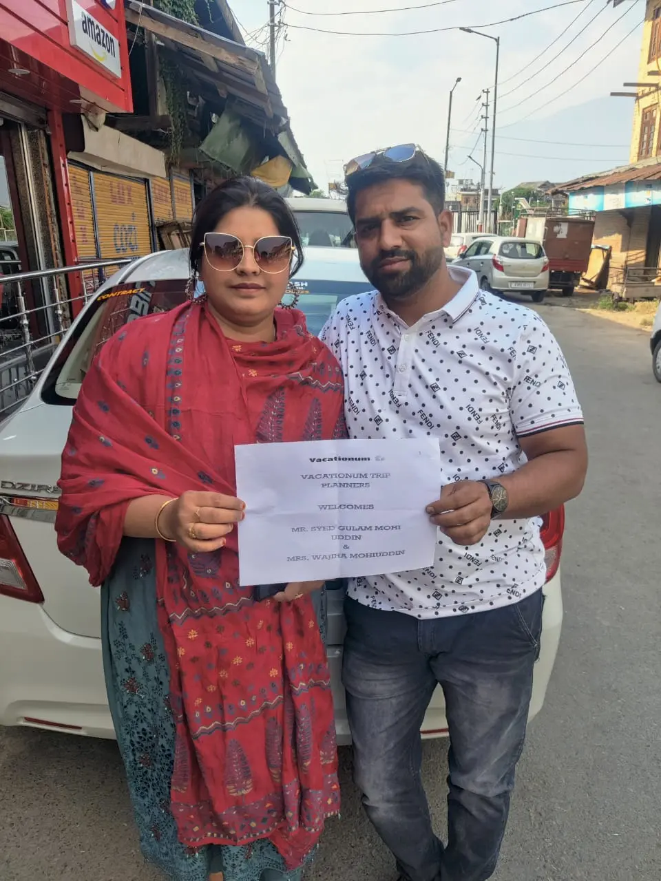 Couple holding Vacationum Trip Planners welcome placard at Srinagar airport.